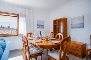 Un coin repas avec une table en bois dressée pour quatre personnes, des chaises avec des sièges rembourrés, un buffet en bois et deux tableaux accrochés au mur.