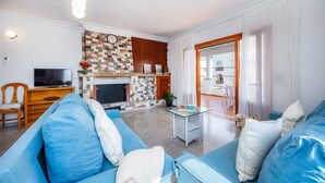 A living room with a television, blue sofa, fireplace, and a dining area visible through an open door. - Apartment 'Apartamento Cabrera' with Private Terrace, Wi-Fi and Air Conditioning (Colònia de Sant Jordi)