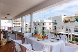 Ein Balkon mit weißen Tischen und Stühlen, ein Frühstücksaufenthalt mit Tellern, Gläsern und Orangensaft, und Blick auf Gebäude im Hintergrund.