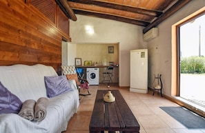 A cozy room with a wooden ceiling, a sofa with cushions, a wooden table, a washing machine, and a refrigerator.