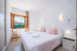 A hotel room with a bed, two bedside tables with lamps, a chair, a window with curtains, and a view of buildings outside.