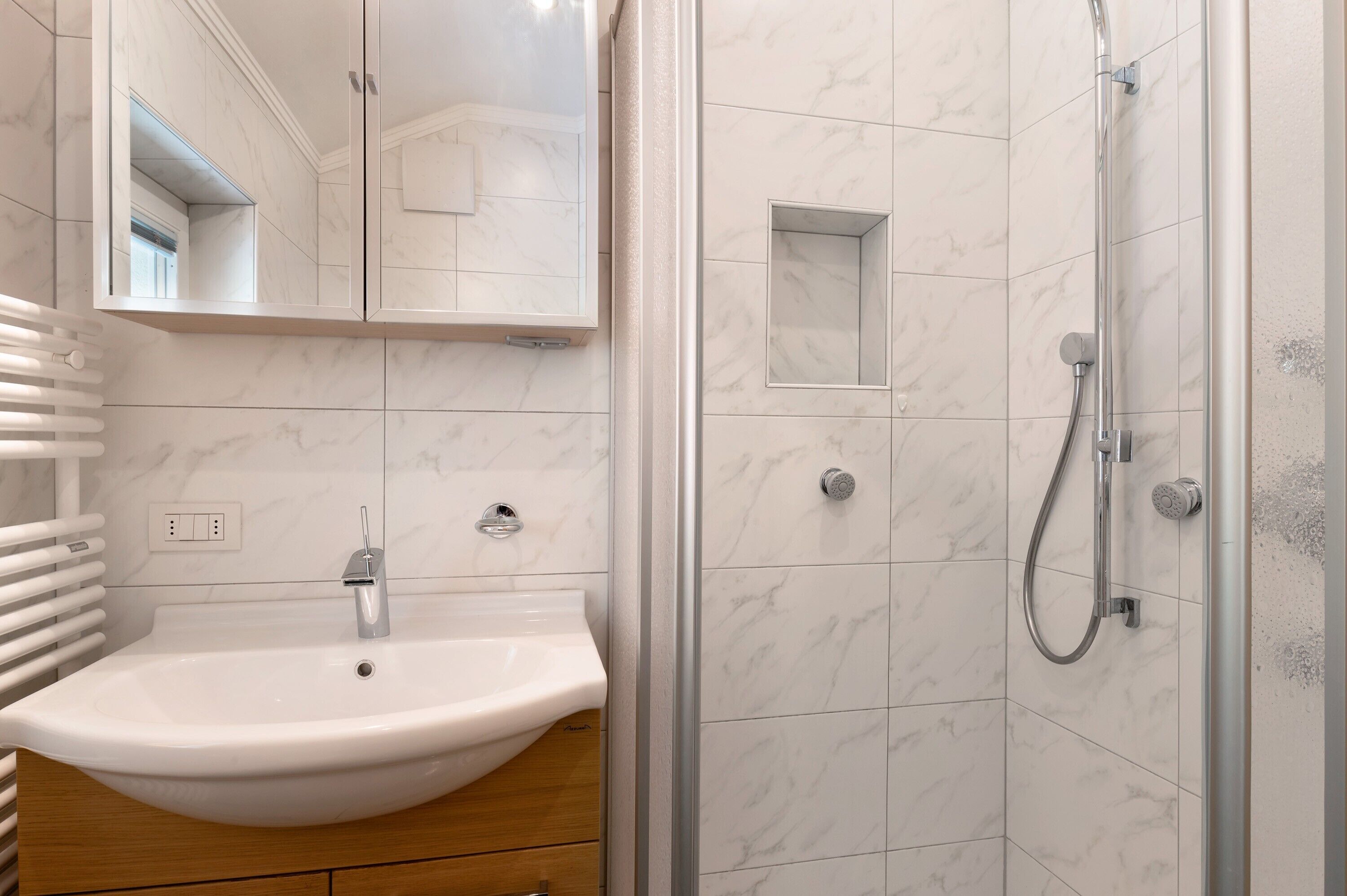Une salle de bain avec un lavabo, un miroir, une douche et des murs carrelés.