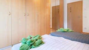 A bedroom with a bed, green towels, wooden wardrobe, and a mirror.