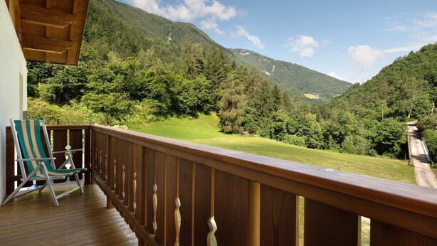 A wooden deck with a view of a lush green valley and mountains.