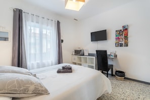 Ett hotellrum med en säng, ett skrivbord med en dator, en TV och en anslagstavla som hänger på väggen.
