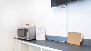 A kitchenette with a microwave, a small refrigerator, a coffee maker, and a flat-screen TV mounted on the wall. - L'Oranger room with shared garden, Wi-Fi and air conditioning (Perpignan)