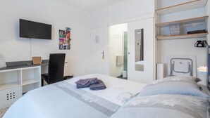 A hotel room with a bed, a desk, a chair, a TV, a bathroom mirror, and a shelf with personal items. - L'Oranger room with shared garden, Wi-Fi and air conditioning (Perpignan)