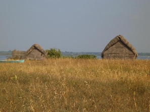 Two thatched-roof huts in a grassy field with a body of water in the background.