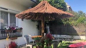 A patio with a thatched umbrella, outdoor furniture, and potted plants. - Canigou Et Jo room with shared garden, Wi-Fi and air conditioning (Perpignan)