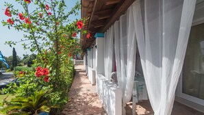 A covered outdoor area with a pathway, white curtains, and a plant with red flowers. - Apartment 'Andromaches Single Studio' with Sea View, Wi-Fi and Air Conditioning (Corfu)