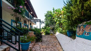 A stone-paved courtyard with a staircase, potted plants, and a white wall with a mural. - Apartment 'Andromaches Single Studio' with Sea View, Wi-Fi and Air Conditioning (Corfu)