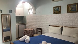 A bedroom with a bed, a small table, a chair, a mirror, and a kitchenette. - Apartment 'Andromaches Single Studio' with Sea View, Wi-Fi and Air Conditioning (Corfu)