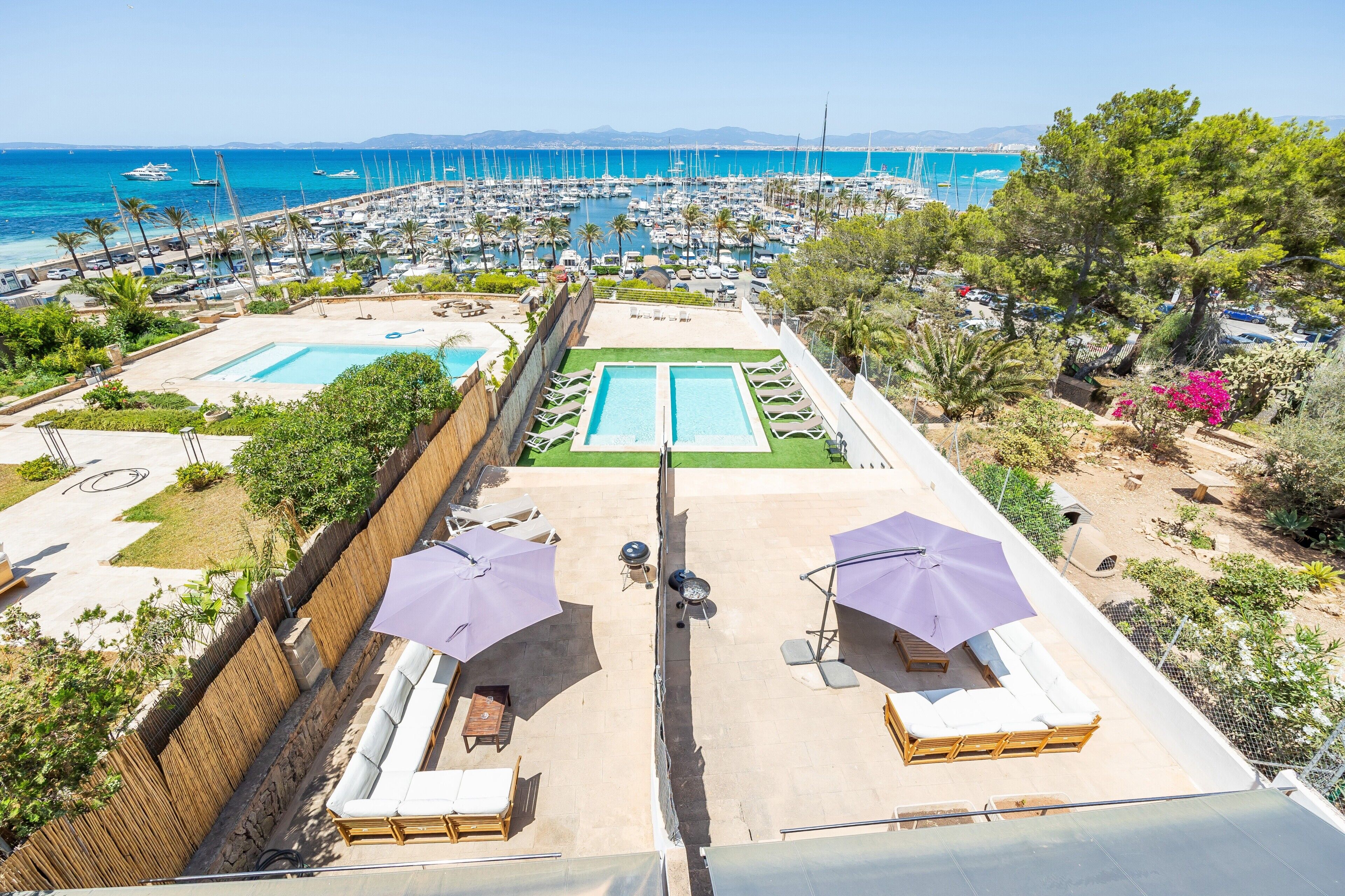 A rooftop pool area with two pools, lounge chairs, umbrellas, and a view of the marina and sea.