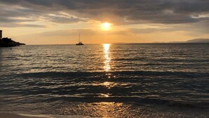 Un coucher de soleil sur une mer calme, avec un bateau et une terre lointaine à l’horizon.