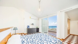 Une chambre à coucher avec un lit, une commode, une lampe et une vue sur la mer.
