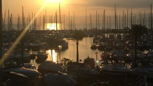 Un port de plaisance où sont amarrés de nombreux bateaux, une étendue d’eau calme et un coucher de soleil en arrière-plan.