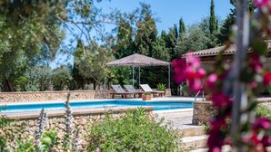 Un área de piscina con sillones de descanso, una pérgola y un muro de piedra.