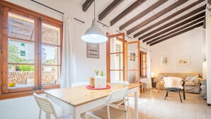 Un comedor con mesa y sillas de madera, una lámpara colgante y vista a una pared de piedra a través de una ventana.