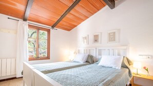 Un dormitorio con dos camas, techo de madera, una ventana con cortinas y cuadros en la pared.