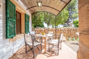 Un espacio de estar techado al aire libre con una mesa, sillas, un muro de piedra y un techo de paja.