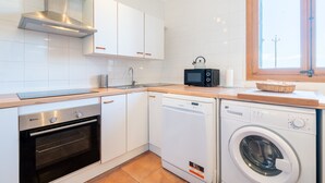 Una cocina compacta con armarios blancos, un extractor de acero inoxidable, un microondas, un lavavajillas y una ventana con vistas.