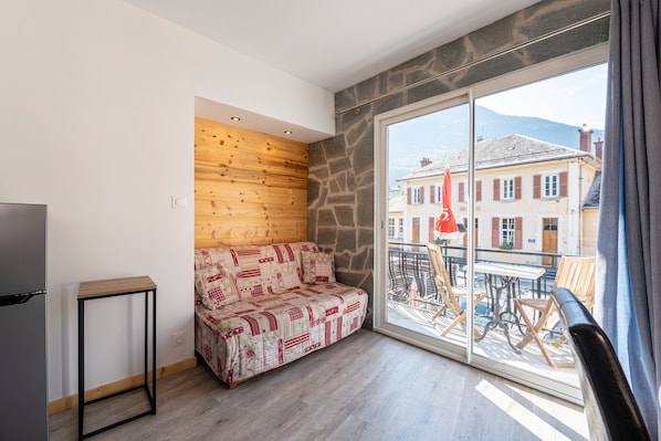 A room with a wooden wall, a sofa, a small table, and a large window with a view of buildings and mountains.