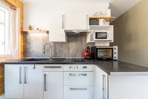 A modern kitchen with white cabinets, a stainless steel range hood, a microwave, an oven, and a coffee maker.