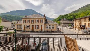 Ein Gebäude mit dem Schriftzug 'MAIRIE', eine Straße mit parkenden Autos und ein Berg im Hintergrund.
