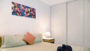 Ett hotellrum med en säng, kuddar, ett sängbord med en lampa och en färgstark, abstrakt tavla på väggen.