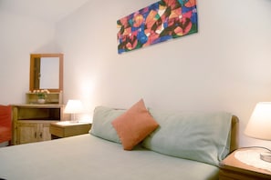 Ein Schlafzimmer mit Bett, Nachttisch, Lampe, Kommode, Spiegel und einem farbenfrohen abstrakten Gemälde an der Wand.