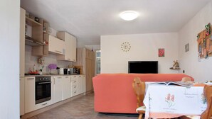 Ett kompakt bostadsutrymme med ett litet kök, en soffa, ett matbord med stolar och en tv.