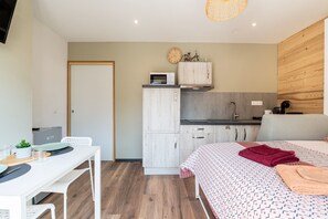 Une pièce de taille modeste comprenant un lit, une petite kitchenette, un coin repas et une porte blanche.