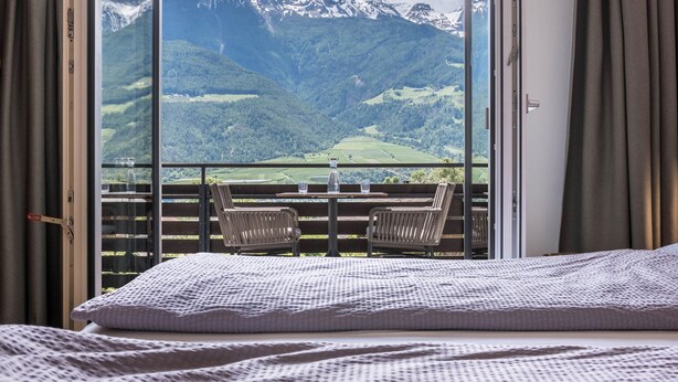 A balcony with a table and chairs, a bed, and a mountain view.