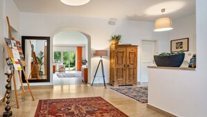 A spacious hallway with a wooden floor, a large rug, a wooden cabinet, a lamp, and a potted plant.