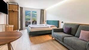 A hotel room with a bed, a sofa, a wooden table, and a TV.