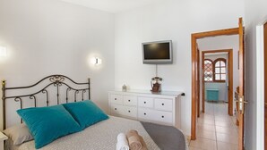 Un dormitorio con cama, cómoda, televisor y puerta que da a otra habitación.
