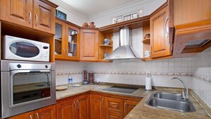 Una cocina con armarios de madera, electrodomésticos de acero inoxidable, un lavamanos y un salpicadero de azulejos.