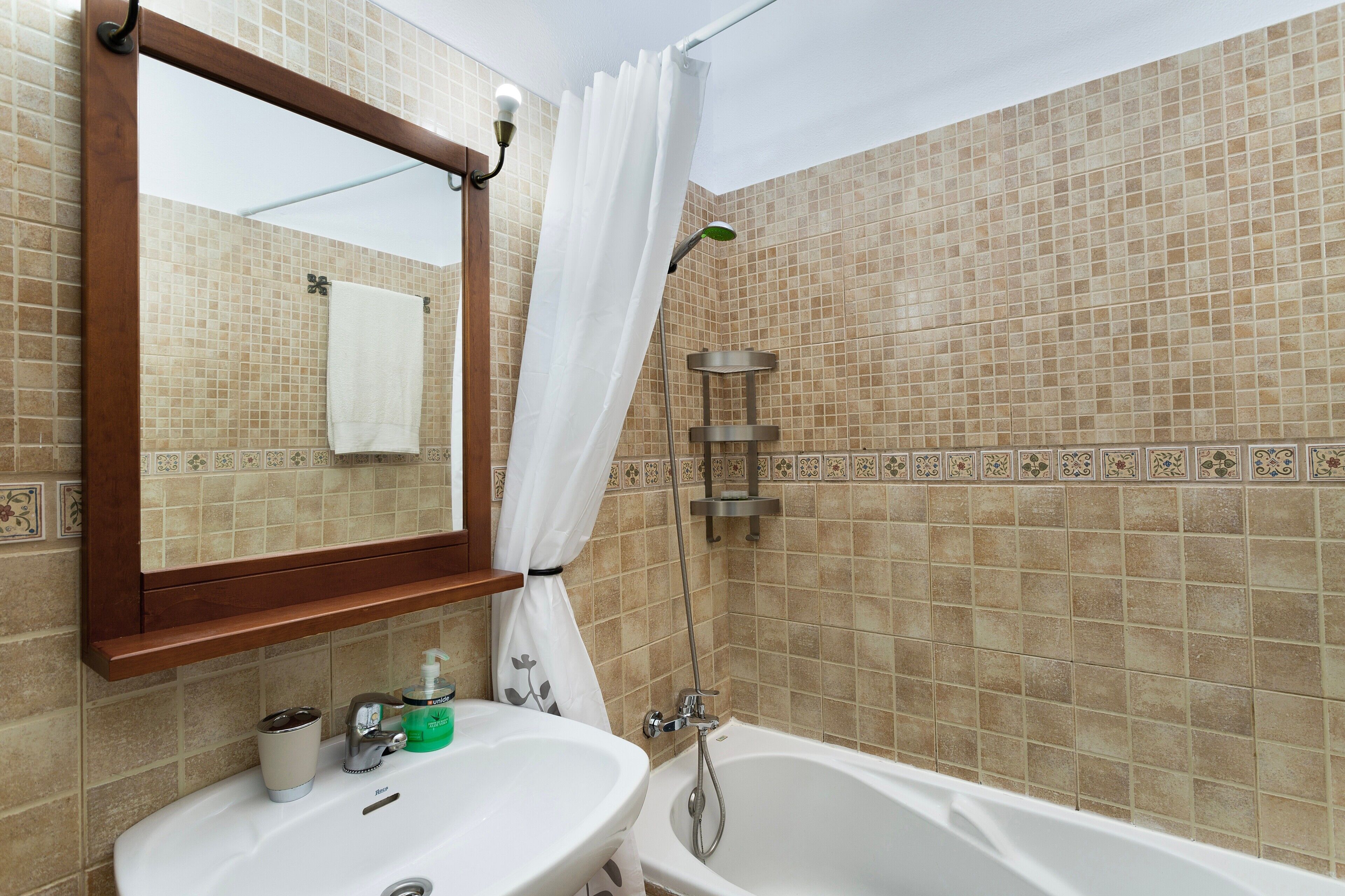 Une salle de bain avec un lavabo, un miroir, une douche et des murs carrelés.