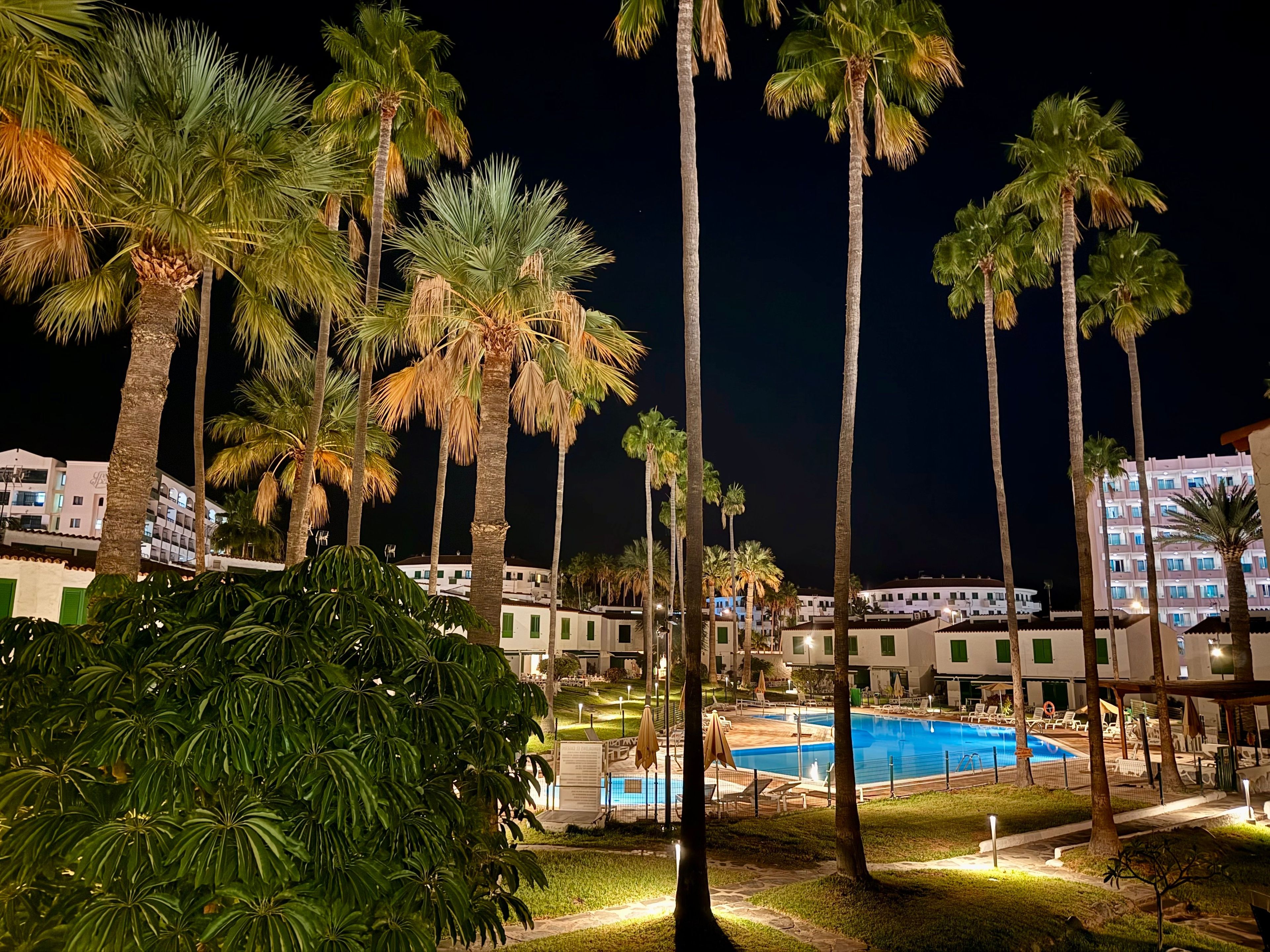 Un resort nocturno con piscina, palmeras y edificios de hotel.