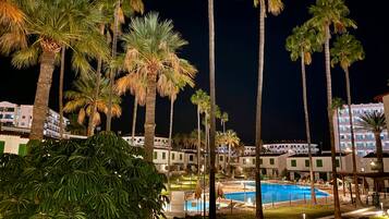 Ein Resort bei Nacht mit Schwimmbad, Palmen und Hotelgebäuden.