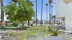 Un patio con mesa y sillas, rodeado de palmeras y un edificio de fachada blanca.