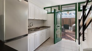 Una cocina con gabinetes blancos, un refrigerador de acero inoxidable, una encimera de granito y una puerta verde que da a un área exterior.