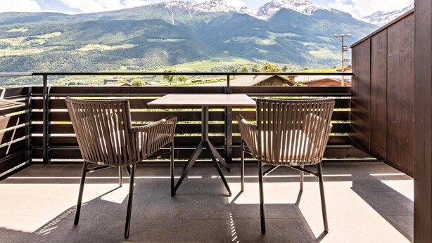 Un balcón con dos sillas y una mesa, con vista a un paisaje montañoso.