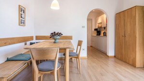 A dining area with a wooden table, chairs, a bench, and a vase of flowers. There is a kitchen visible in the background. - Apartment 'Kortscherhof Apt Typ 3' with Mountain View, Shared Garden and Wi-Fi (Silandro)