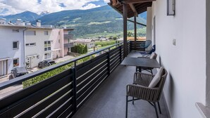A balcony with a table and chairs, a view of a town and mountains, and a railing. - Apartment 'Kortscherhof Apt Typ 3' with Mountain View, Shared Garden and Wi-Fi (Silandro)