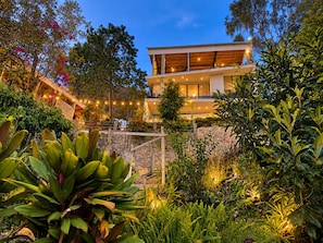 A modern two-story building with a stone retaining wall and lush greenery.