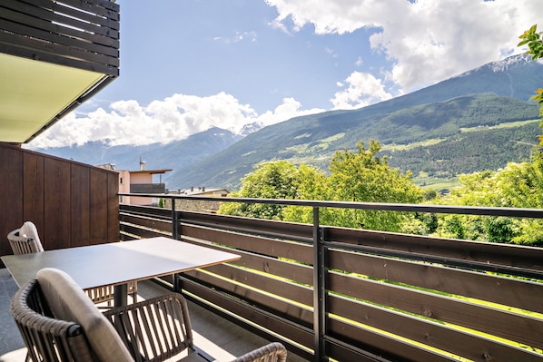 A balcony with a table and chairs, a wooden railing, and a view of a mountain range.