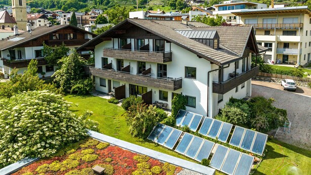 Ein modernes Gebäude mit mehreren Balkonen, Solaranlagen und einem üppigen Garten.