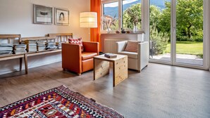 A modern living room with a wooden floor, a sofa, a chair, a coffee table, and a view of a garden through large windows.