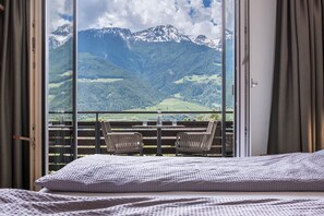 Varanda com mesa, cadeiras, uma cama e vista para as montanhas.